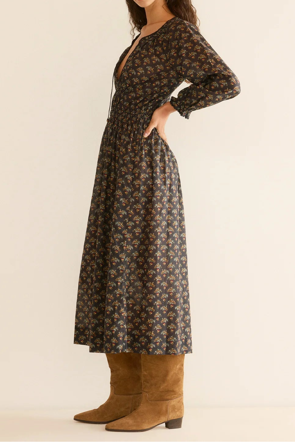 Woman wearing a long floral dress with brown boots on a beige background