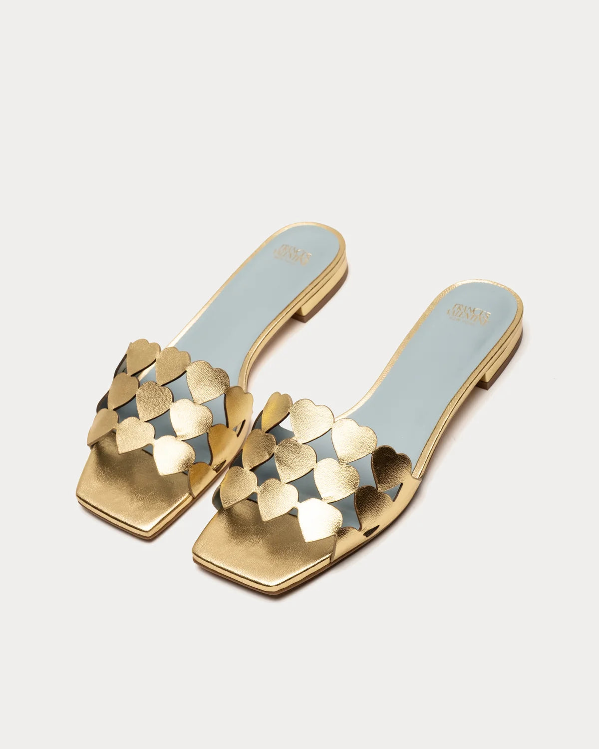 A pair of gold square-toe mule sandals with metallic gold heart-shaped cutout straps and a light blue insole, shown on a light gray background.