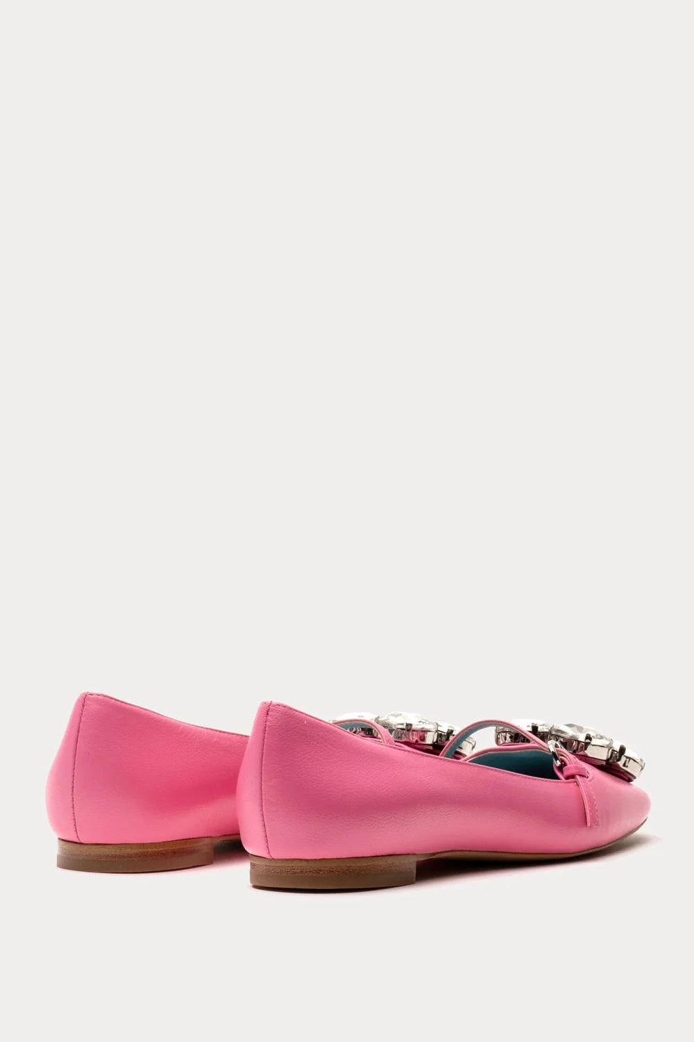 A pair of bright pink leather ballet flats with silver-tone metal hardware across the vamp, shown from a side-rear angle on a light gray background.