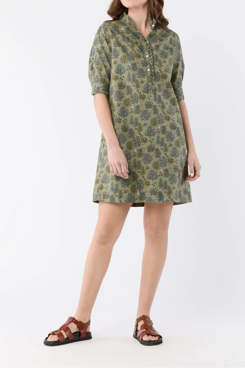 A woman modeling a short-sleeved button-up shirt dress with an olive green and brown floral pattern, paired with brown sandals, against a plain white studio background.
