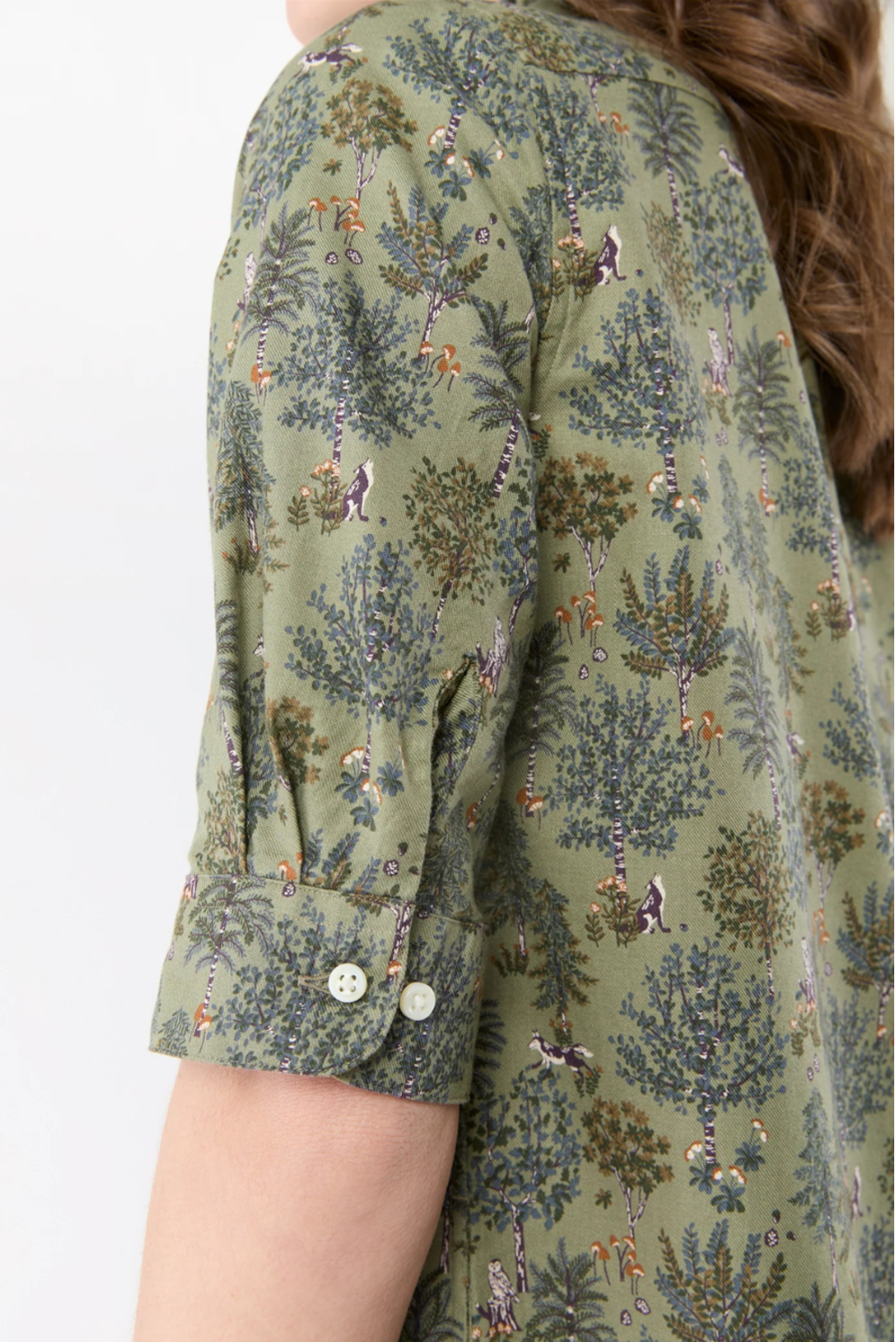 Close-up of a person wearing a sage green short-sleeve shirt with a detailed botanical and animal print, featuring a buttoned cuff.