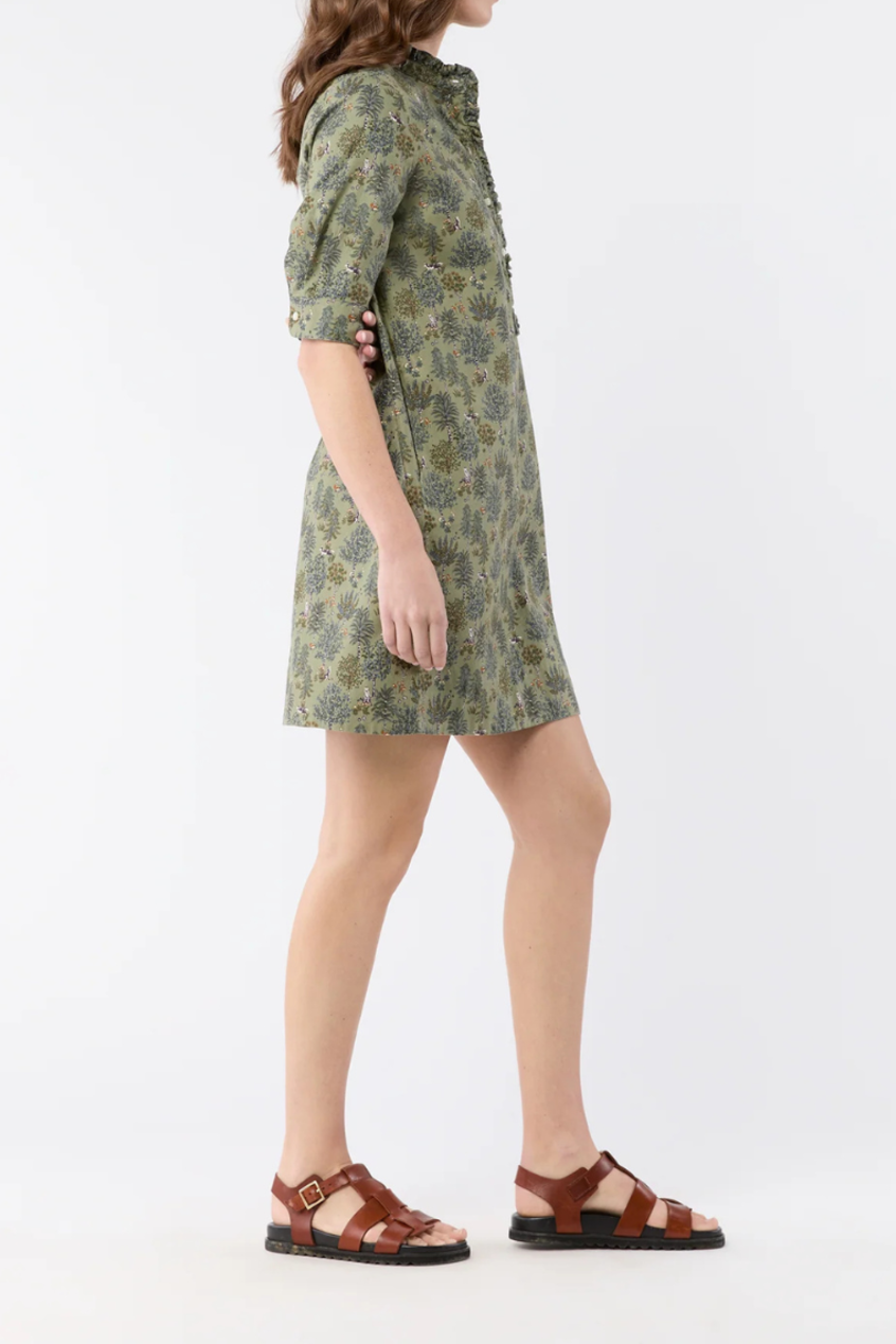 A woman modeling a short-sleeved olive green and brown patterned dress with a high collar, shown from a side profile against a plain white studio background.