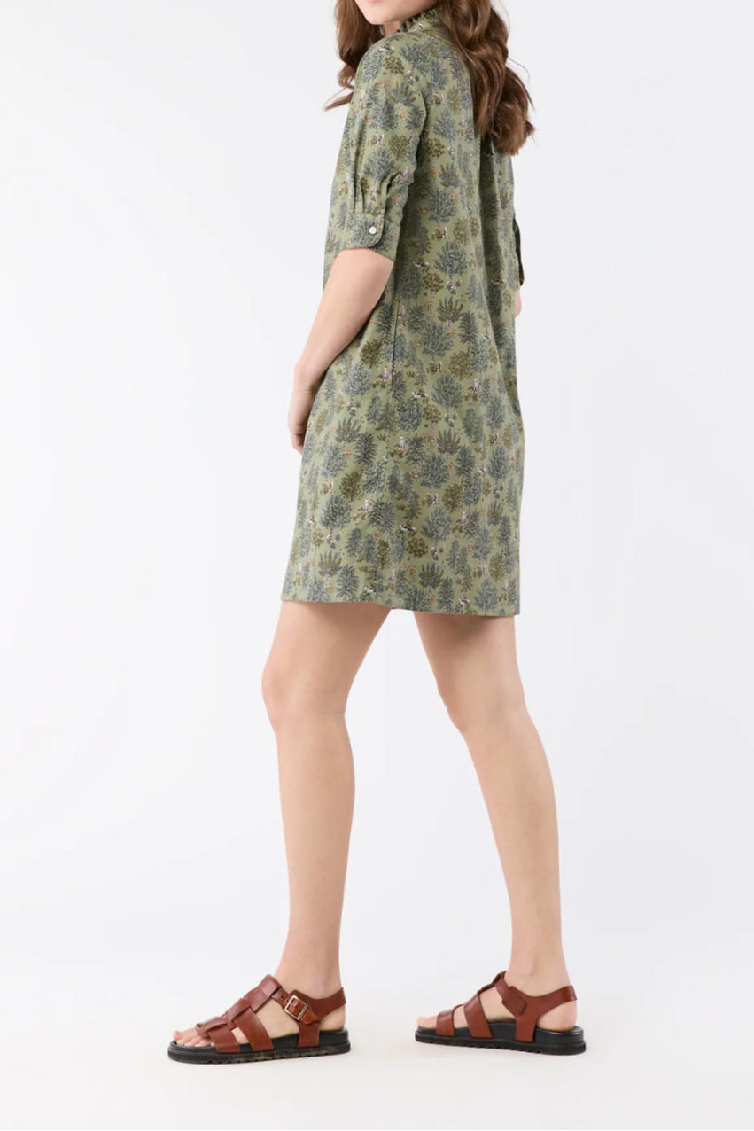 A woman modeling a short-sleeve olive green and brown patterned shirt dress, paired with brown strappy sandals, against a plain white studio background.