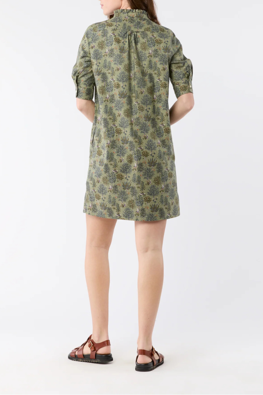 A woman viewed from the back wearing a short-sleeved olive green and brown floral print shirt dress, paired with brown sandals, against a plain white studio background.