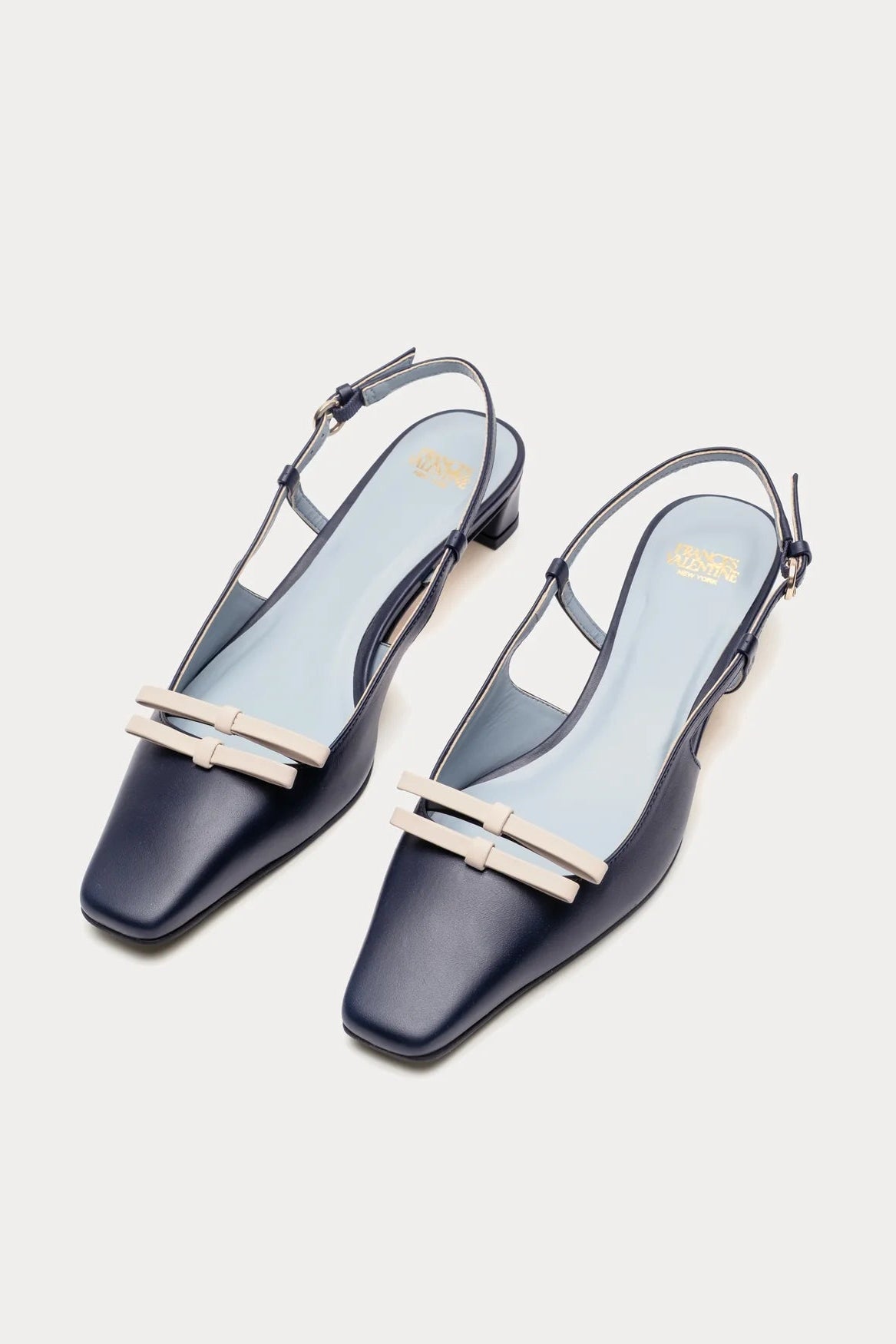 Pair of navy blue slingback shoes with gold accents on a light gray background