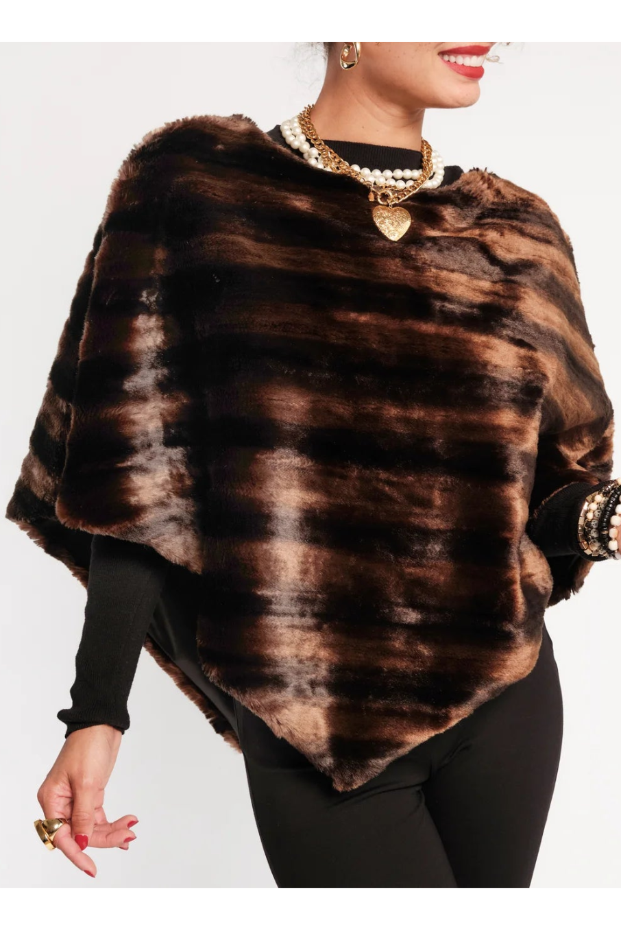 A woman modeling a brown and black faux fur poncho with a tie-dye pattern, styled over a black long-sleeve top and black pants against a plain white background.