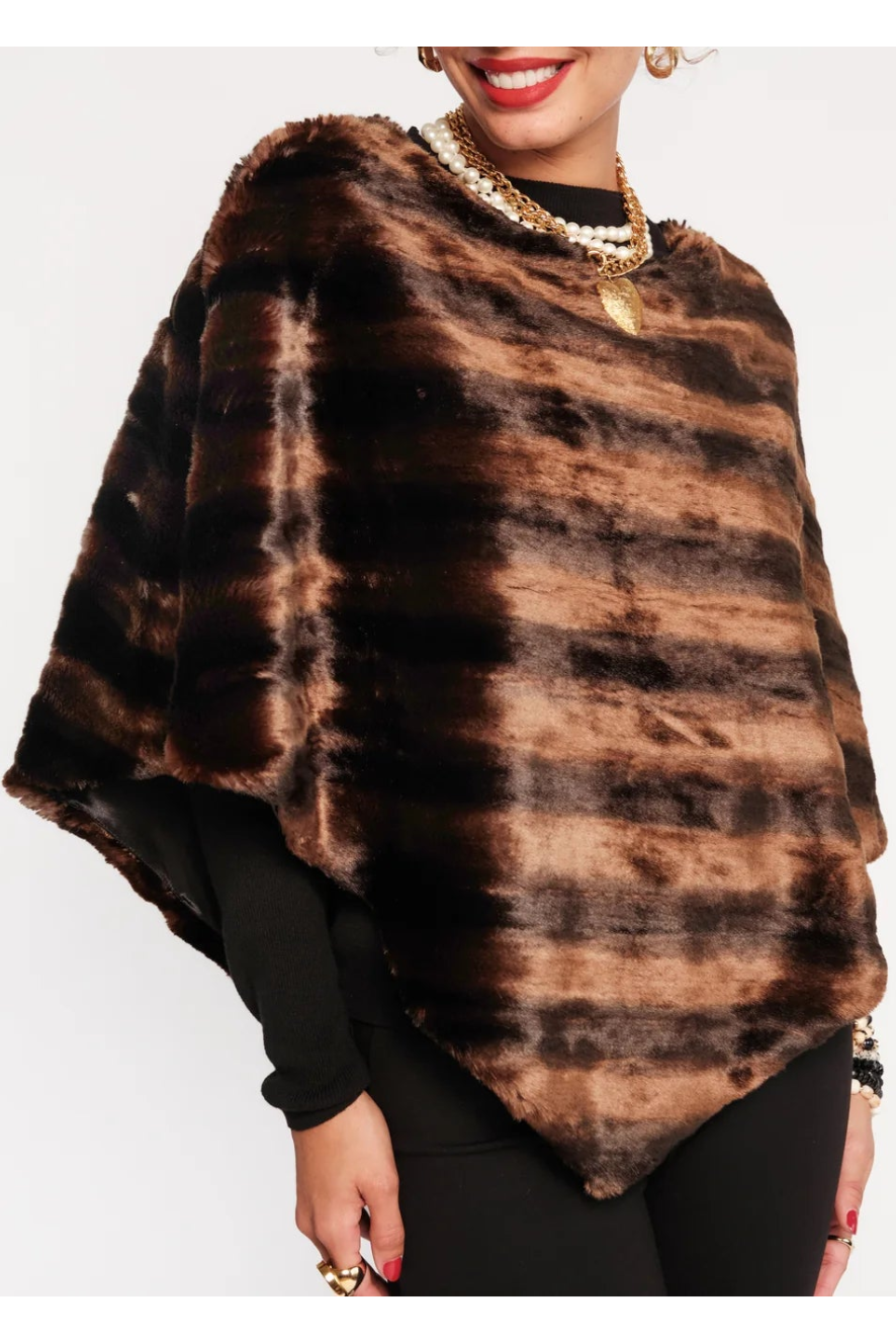 A woman modeling a brown and black faux fur poncho with a tie-dye pattern, styled over a black top and black pants against a plain white background.
