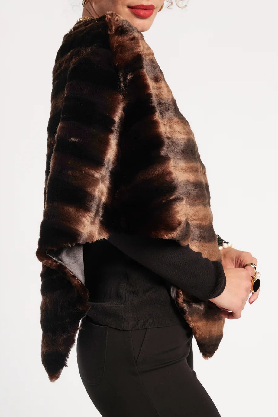 A woman modeling a dark brown and black tiger-striped faux fur wrap or cape jacket, paired with black pants, against a plain white studio background.