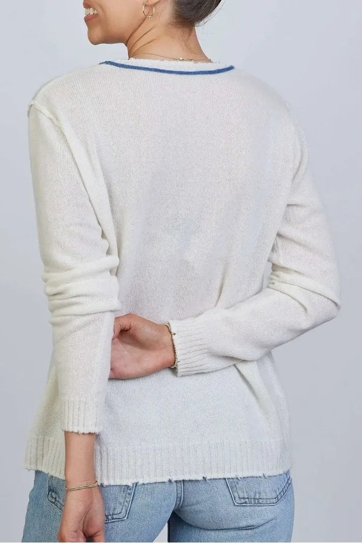 A woman shown from the back wearing a cream-colored knit sweater with a thin blue collar trim, paired with light blue jeans, against a plain light gray background.