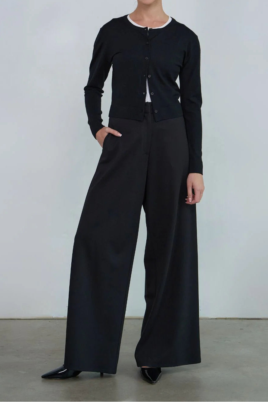 Woman wearing a black outfit with wide-leg pants against a plain background