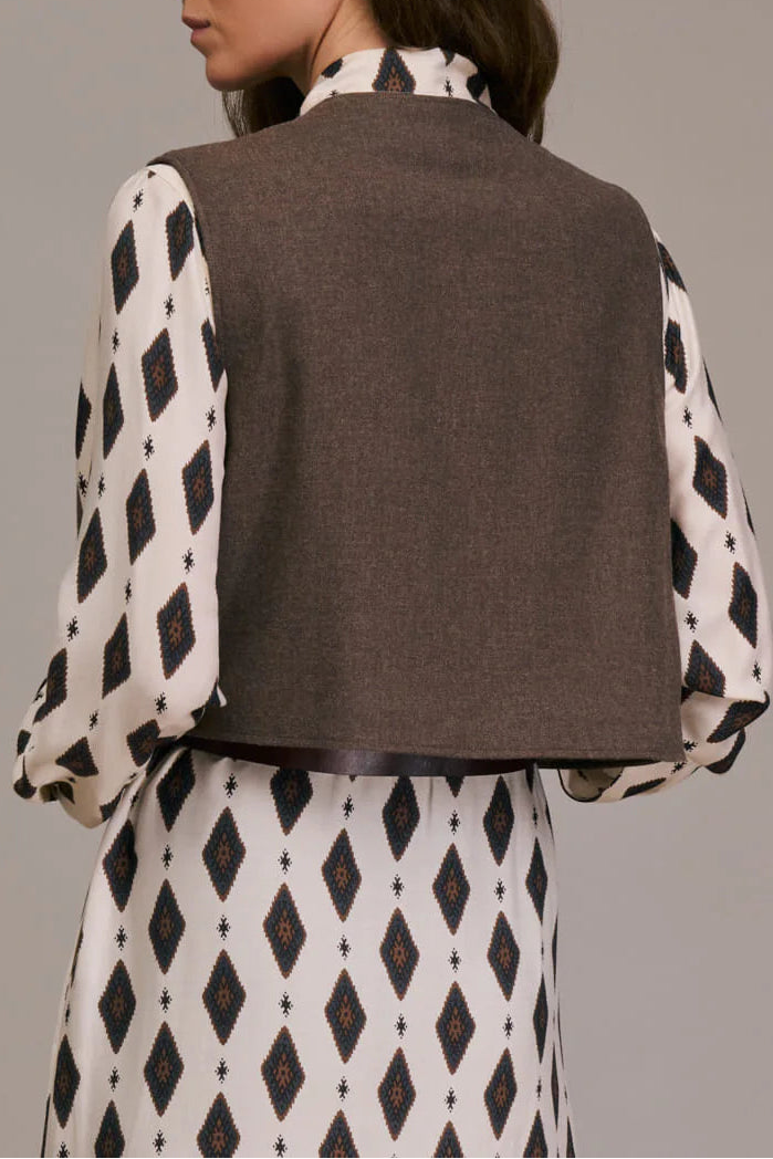 Woman wearing a brown vest over a patterned dress on a plain background