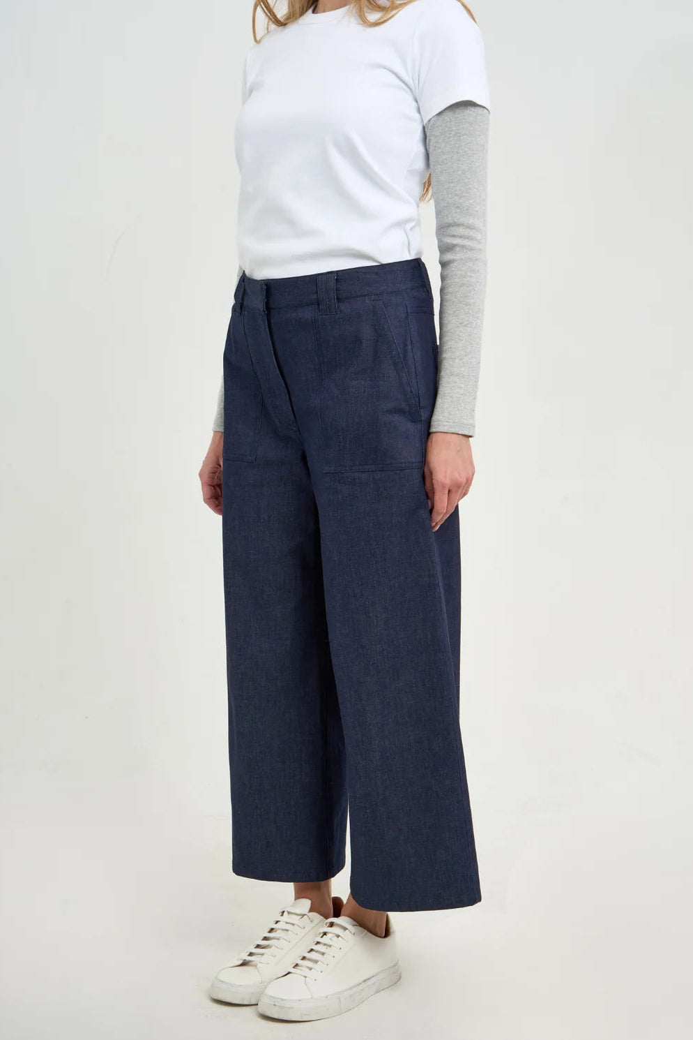 Person wearing navy wide-leg pants with a white top and white sneakers on a light gray background