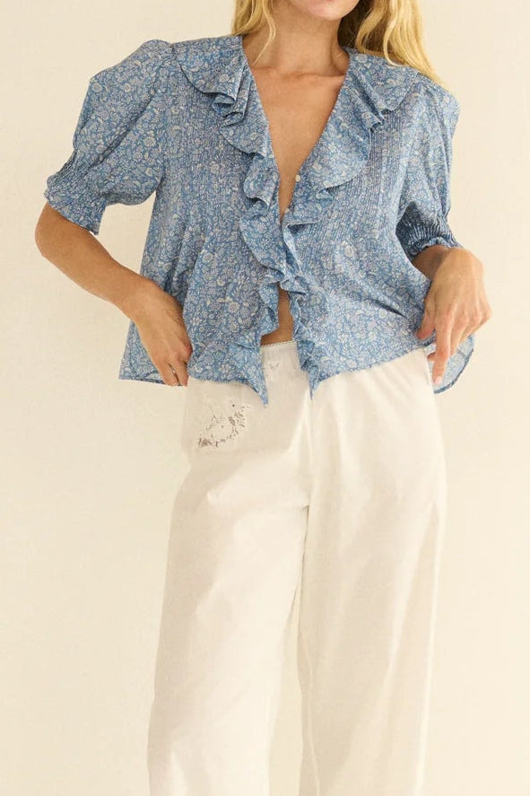 Woman wearing a blue patterned shirt and white pants on a beige background