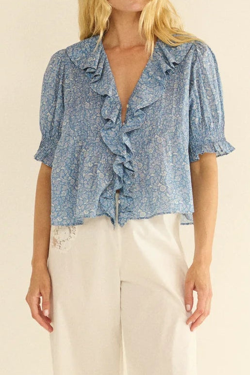 Woman wearing a blue patterned blouse and white pants on a beige background