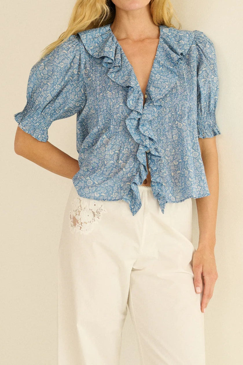 Woman wearing a blue floral blouse with ruffled details on a beige background
