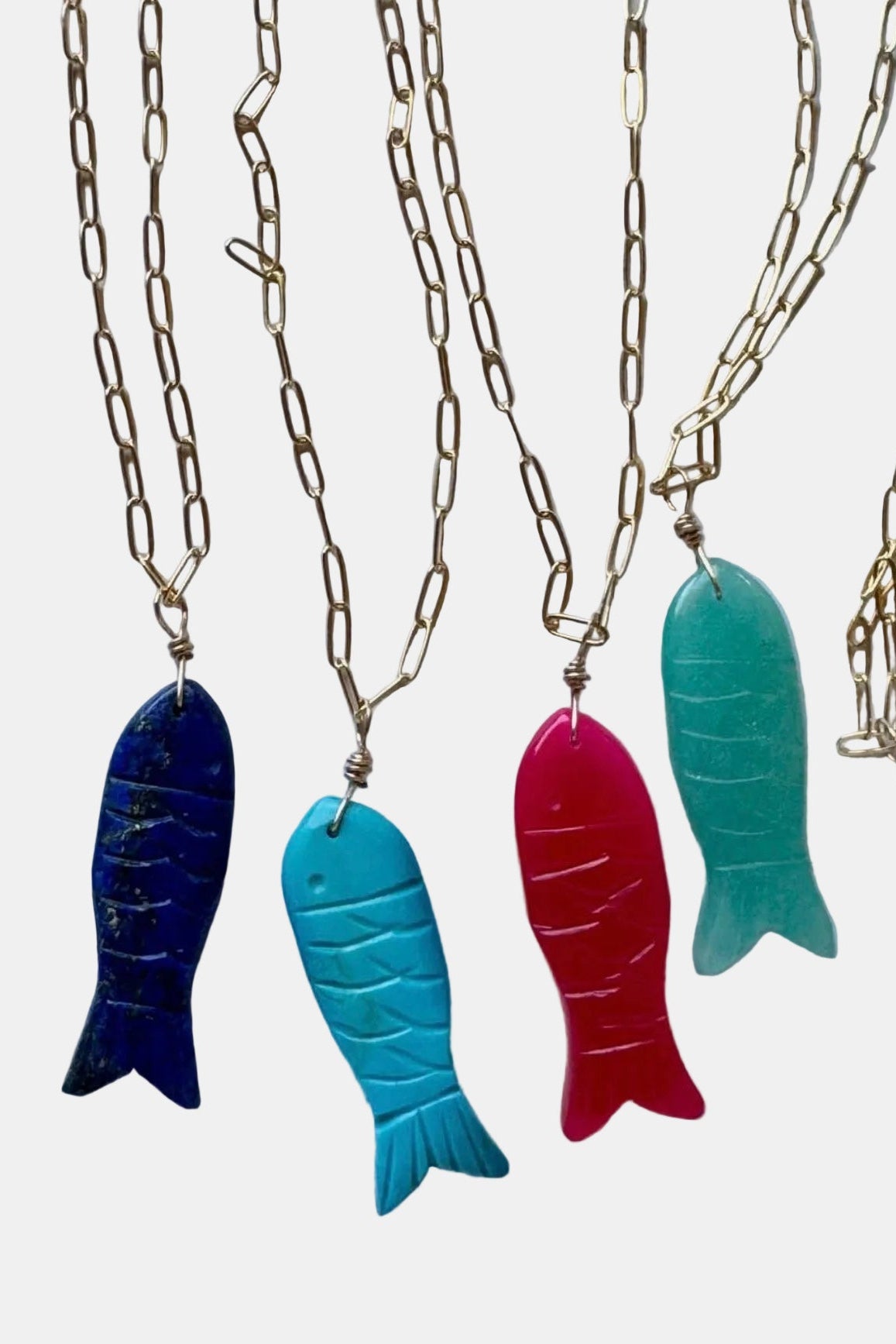 Colorful fish-shaped pendants on gold chains against a marble background