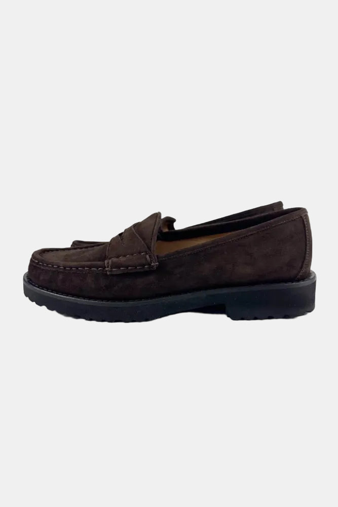 A dark brown suede penny loafer with a tassel detail and a thick black rubber sole, shown in profile against a plain white background.