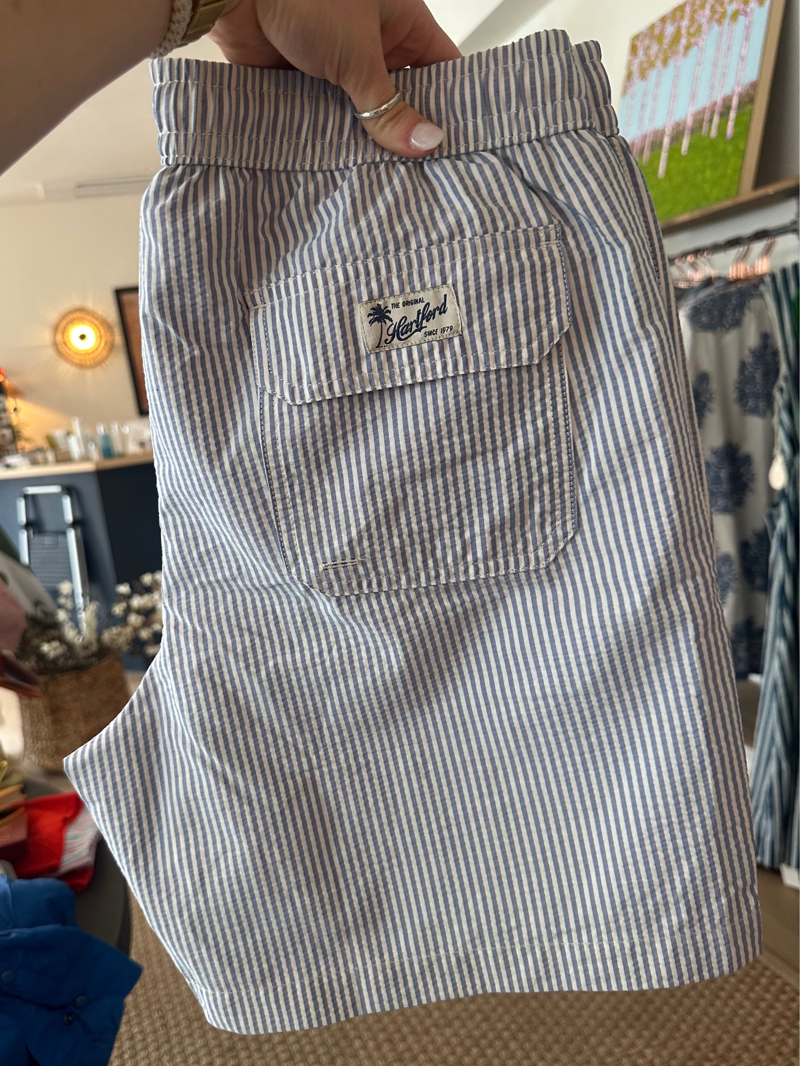 Blue and white striped shorts with a brand logo held by a person in an indoor setting.