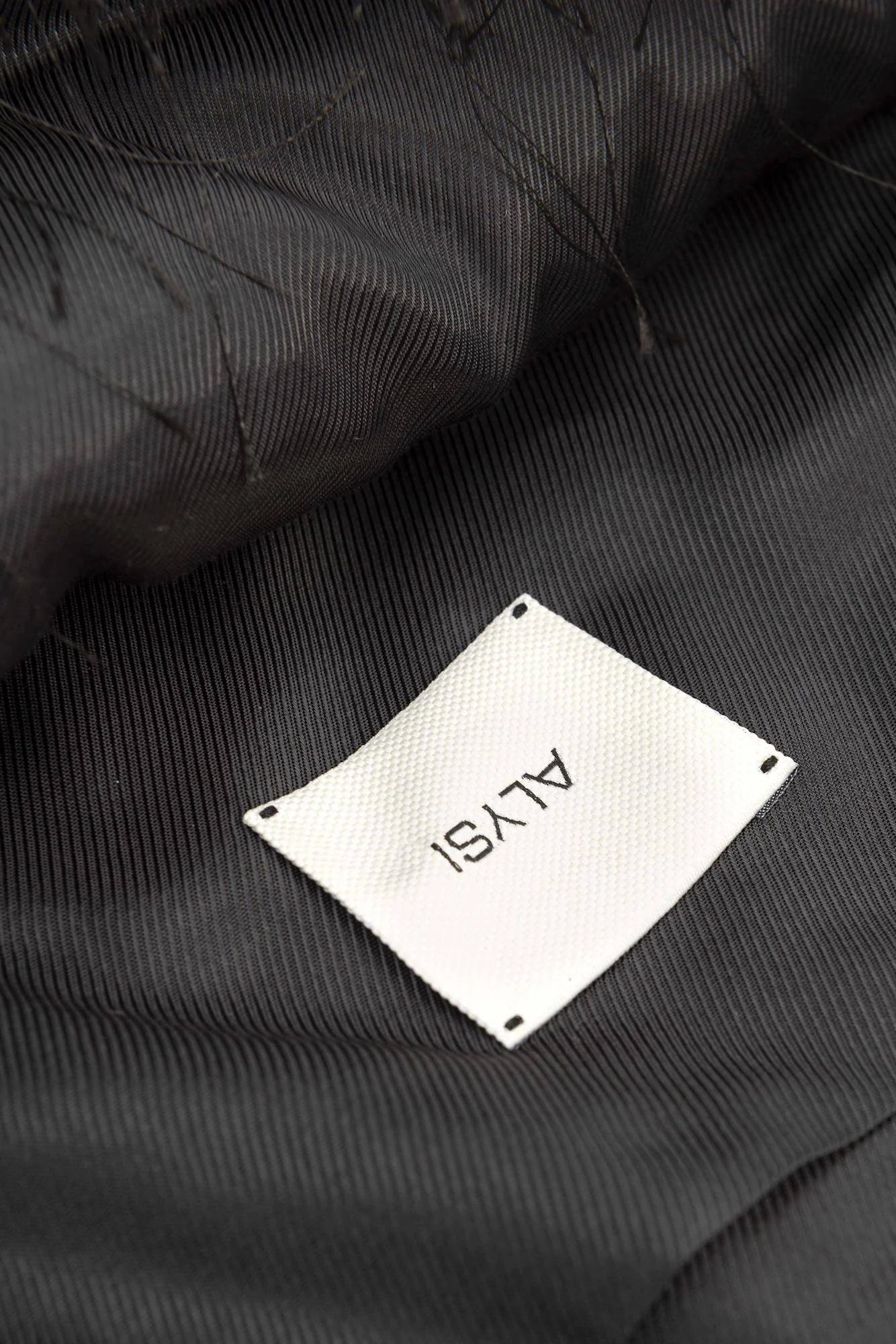 Close-up of a black jacket with a white label displaying 'ALYSI' on a dark background.