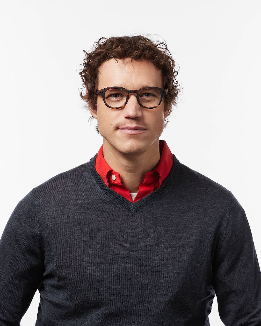 Man wearing a dark gray sweater over a red shirt with a plain background