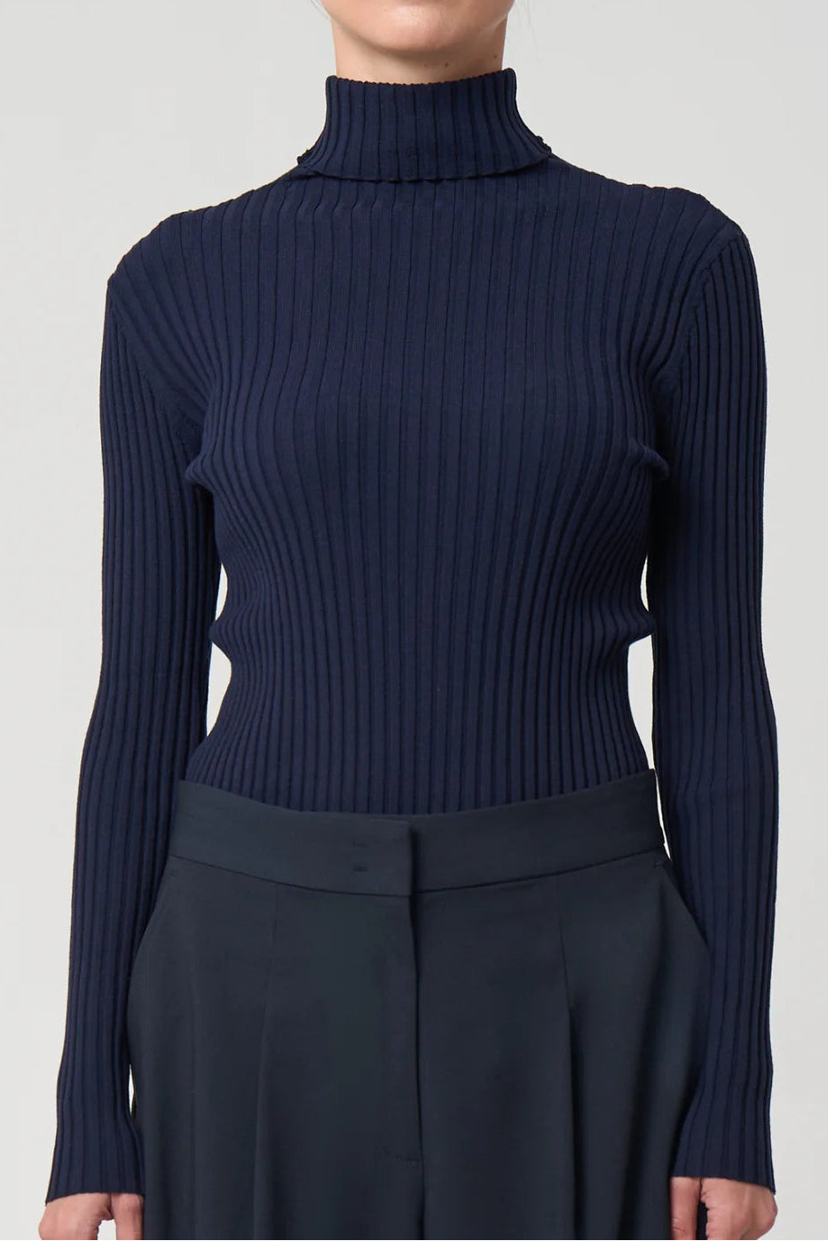 Navy ribbed turtleneck sweater worn by a person on a light gray background