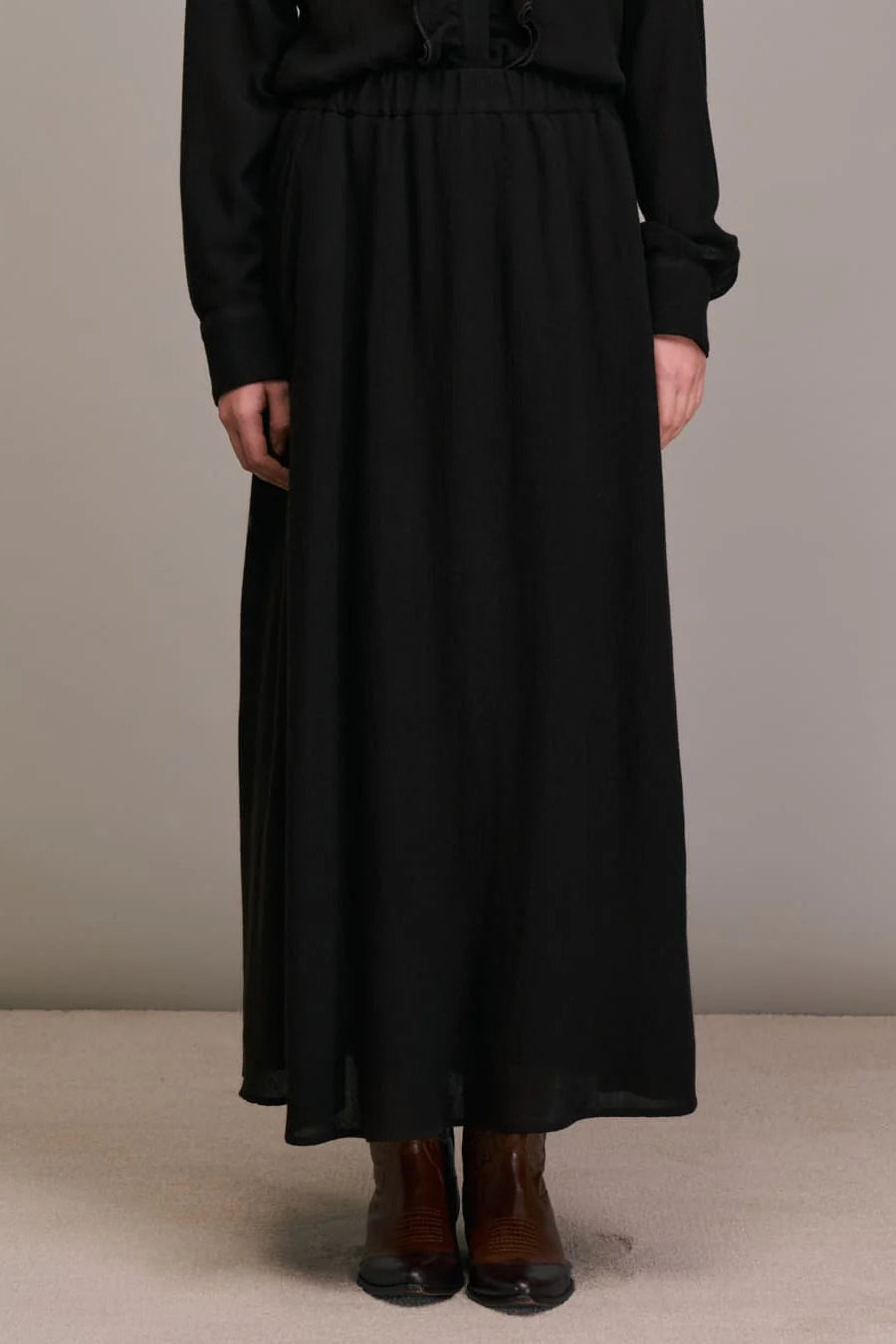 Person wearing a long black skirt with a plain background