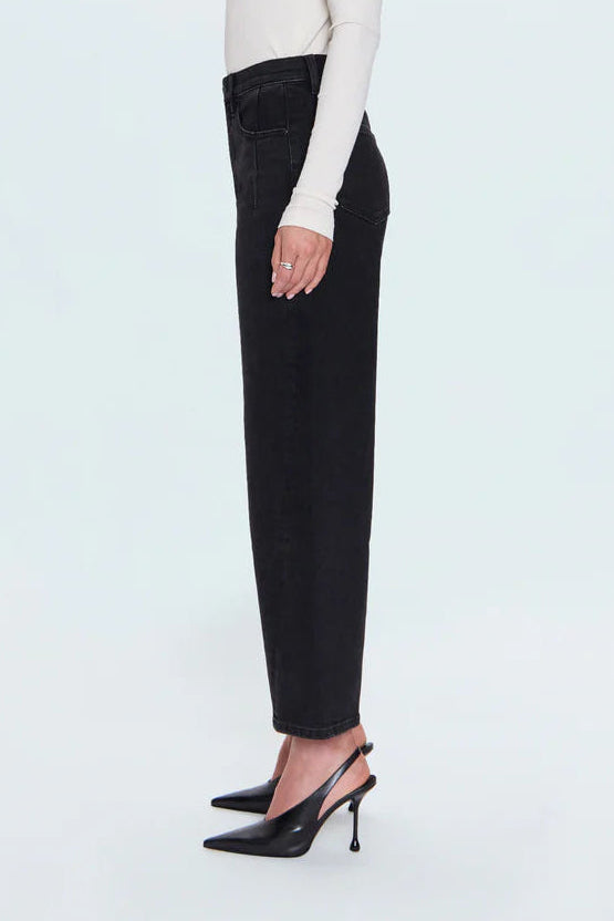 A woman in profile wearing a fitted white long-sleeve top, black wide-leg cropped trousers, and black pointed slingback heels against a light gray studio background.