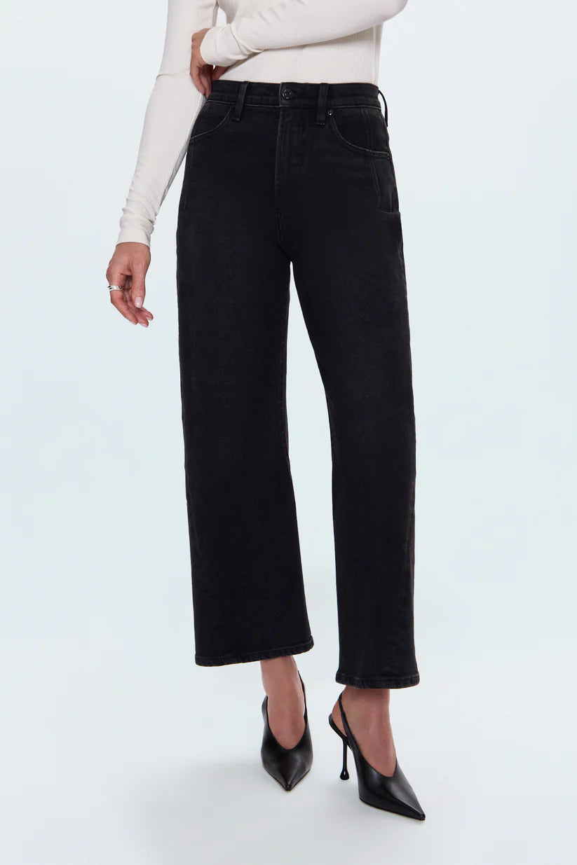 A model wearing black wide-leg cropped jeans, styled with a cream long-sleeve top and black pointed-toe stiletto heels, shown from the waist down on a light gray studio background.