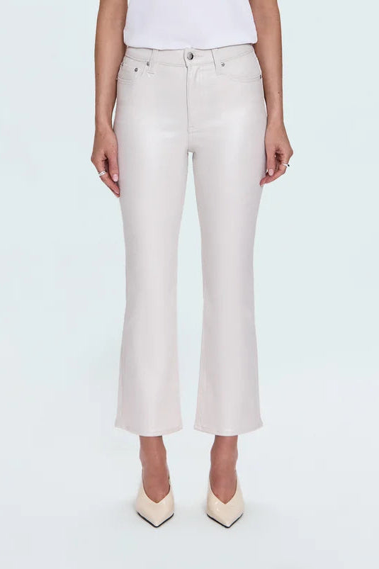 A blonde model stands against a light gray studio background wearing a white short-sleeve crewneck t-shirt, off-white cropped flare jeans, and cream pointed-toe heels.