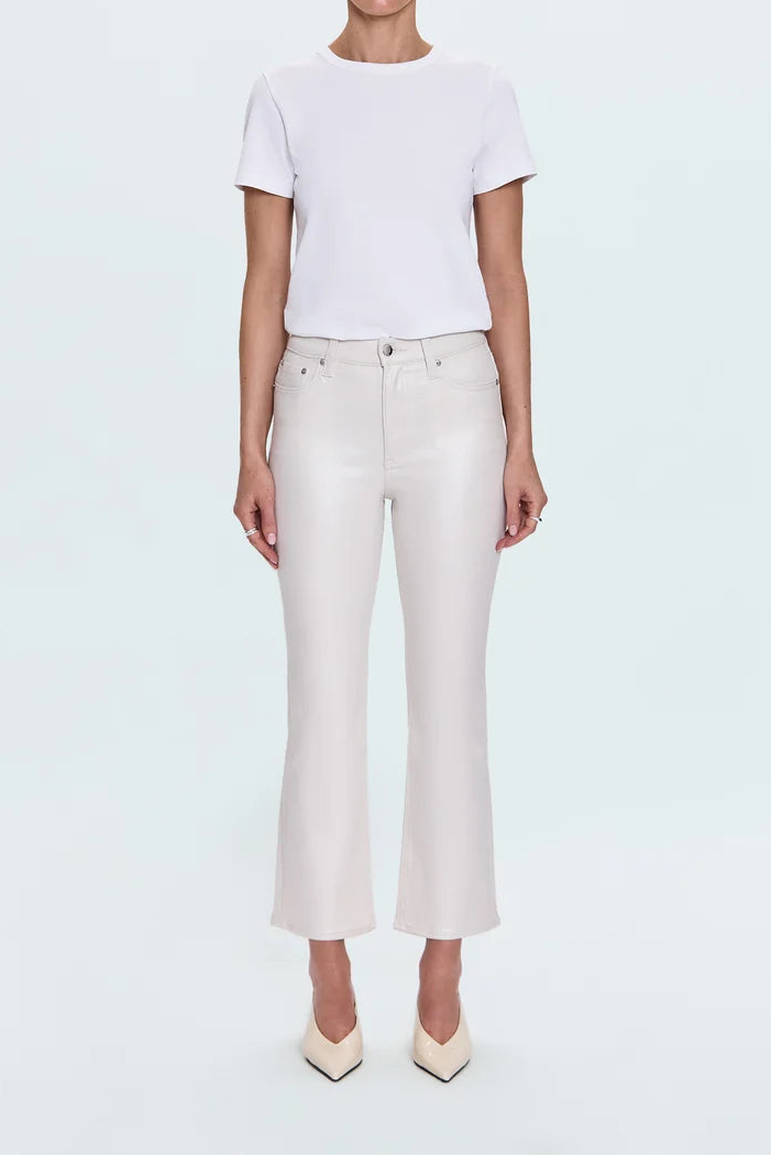A blonde model stands against a light gray studio background wearing a white short-sleeve crewneck t-shirt, off-white cropped flare jeans, and cream pointed-toe heels.