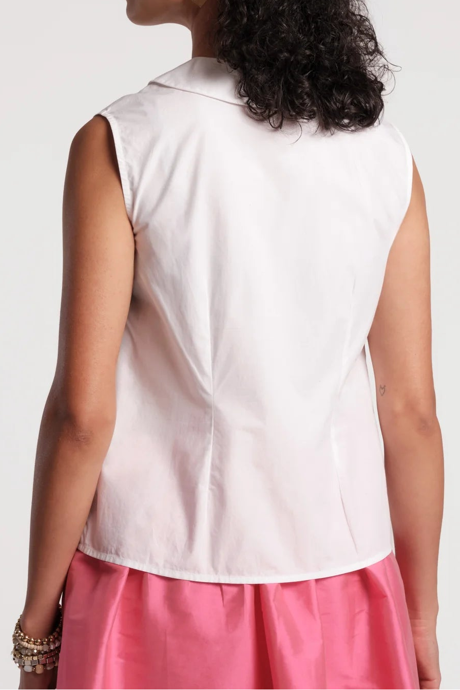 A woman shown from the back wearing a sleeveless white collared top and a pink skirt, photographed against a plain light gray studio background.