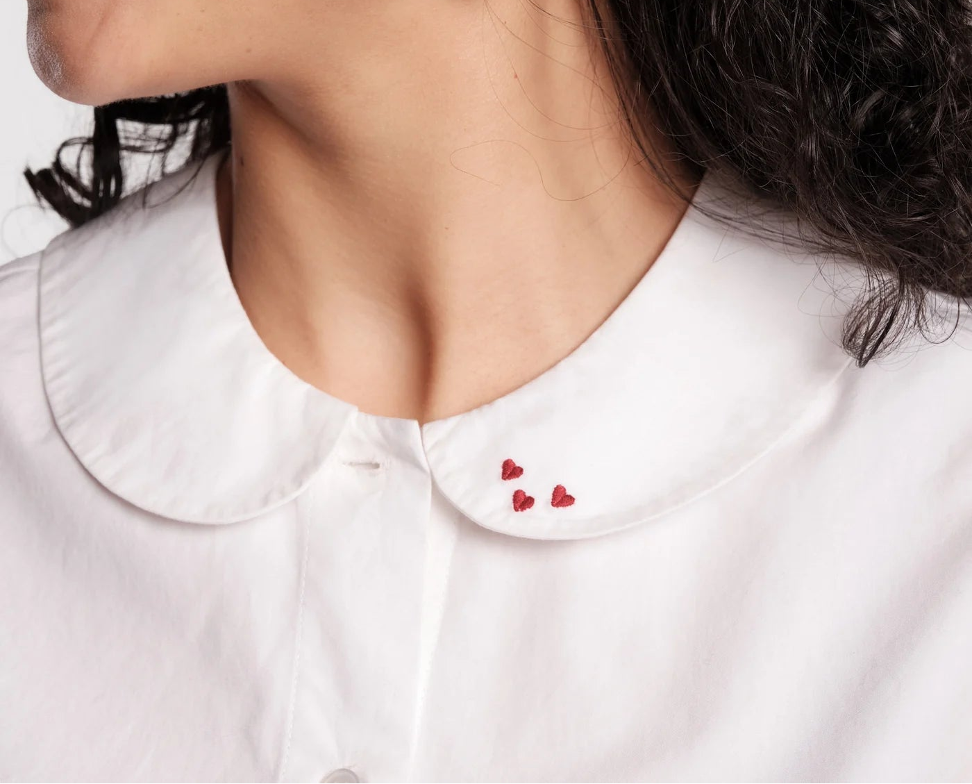 Close-up of a person wearing gold heart-shaped earrings with a white shirt and red lipstick.