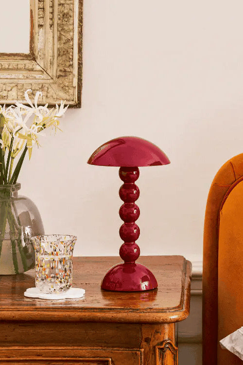 Red table lamp on a wooden side table next to a vase with flowers and a glass.