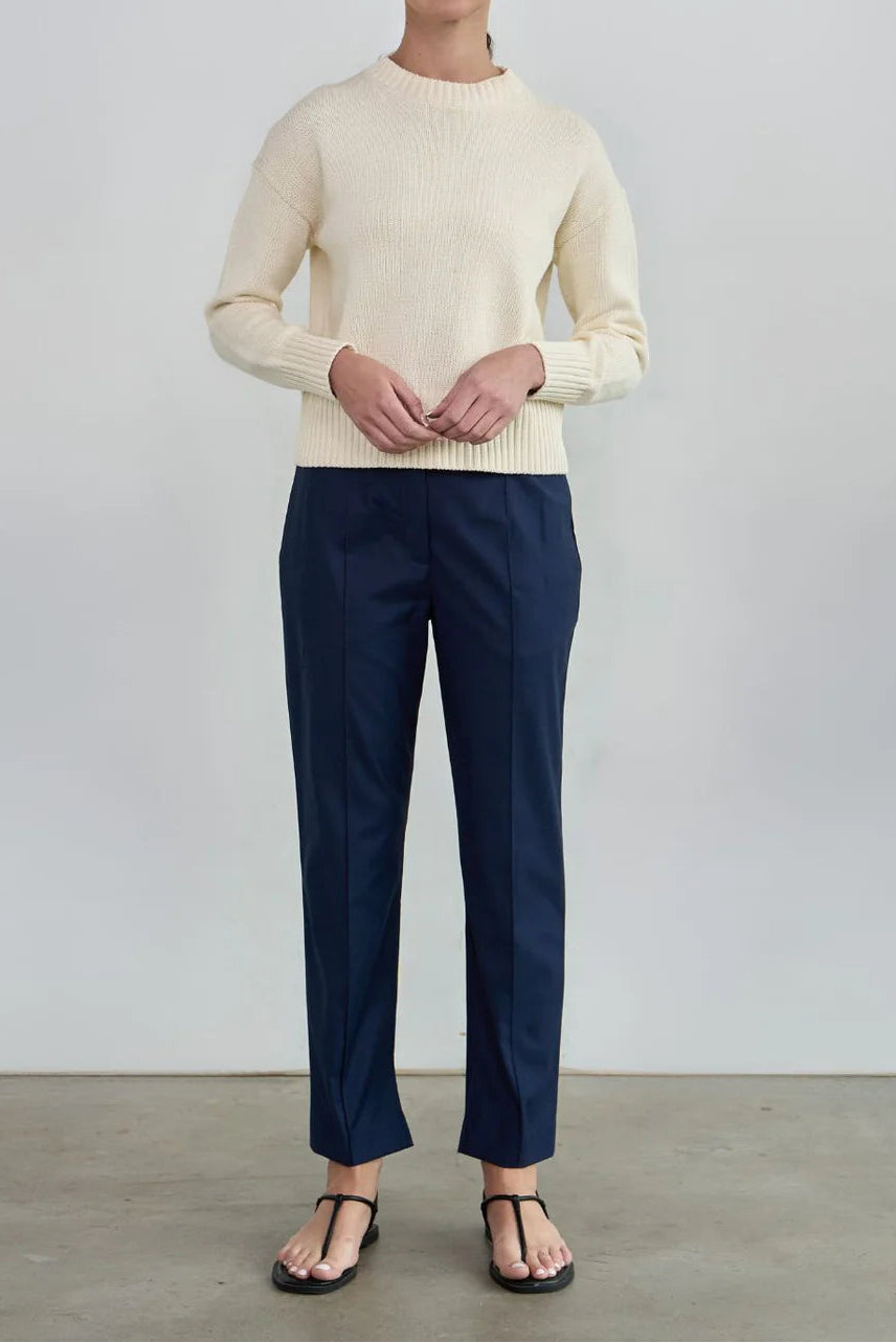Woman wearing a cream sweater and navy pants against a plain background