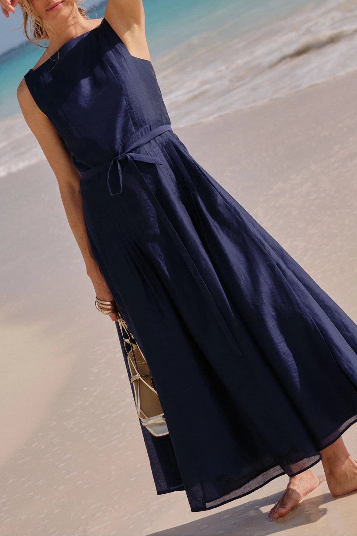 Woman in a navy blue dress standing on a beach with ocean in the background