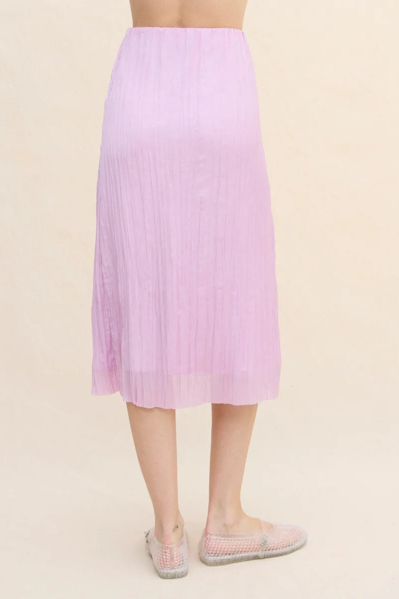 A model is shown from the back wearing a light purple pleated midi skirt and clear jelly shoes against a solid beige background.