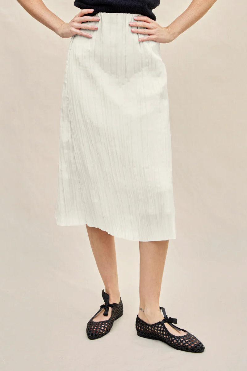 Person wearing a white skirt and black shoes on a beige background