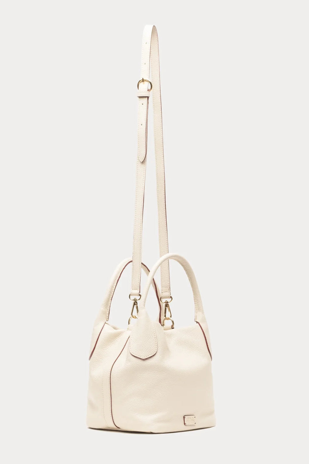 An off-white leather handbag with a long shoulder strap, dual top handles, and gold-tone hardware, shown against a light gray background.