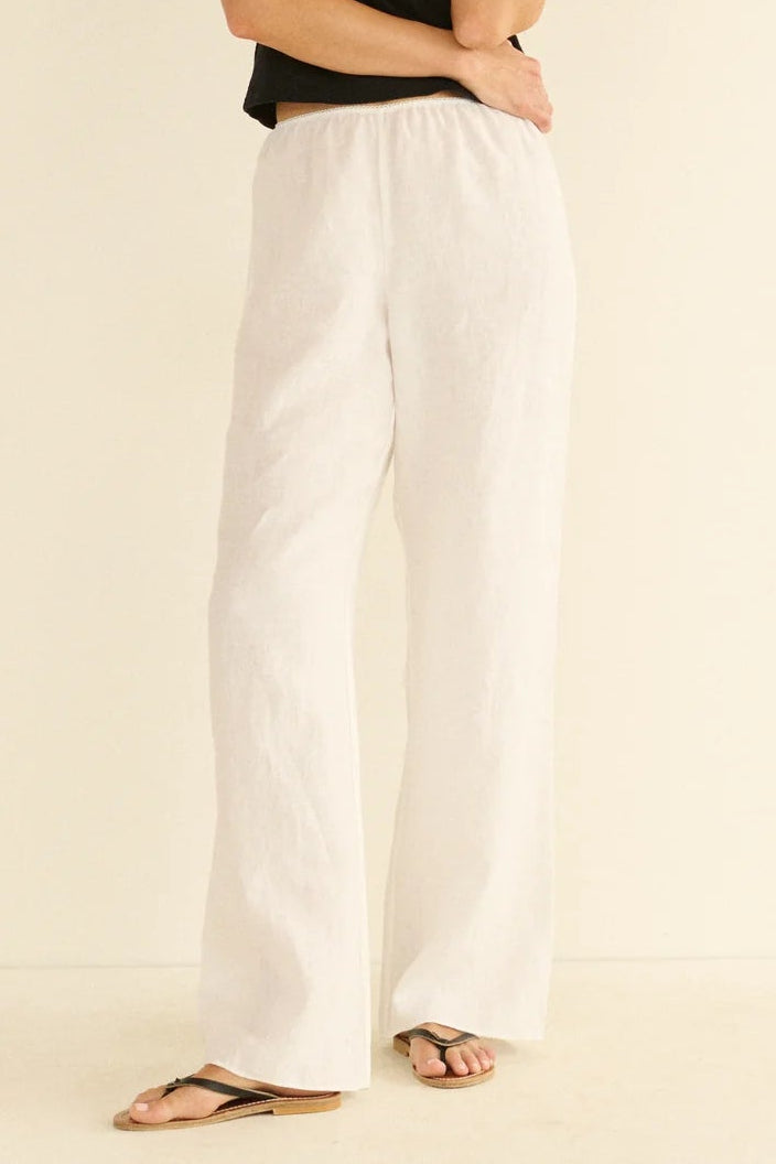 Woman wearing a black top and white pants on a beige background