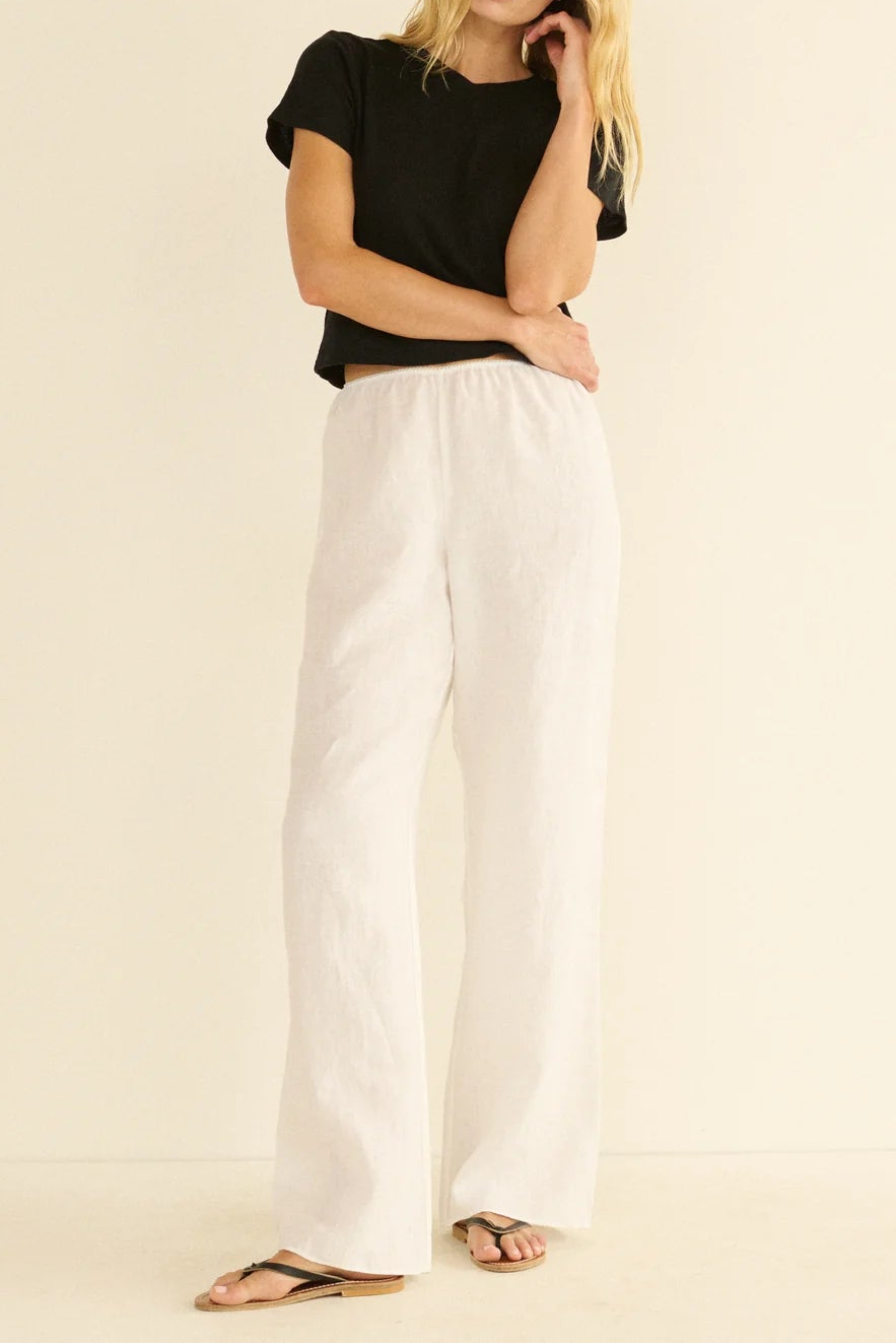 Woman wearing a black top and white pants on a beige background