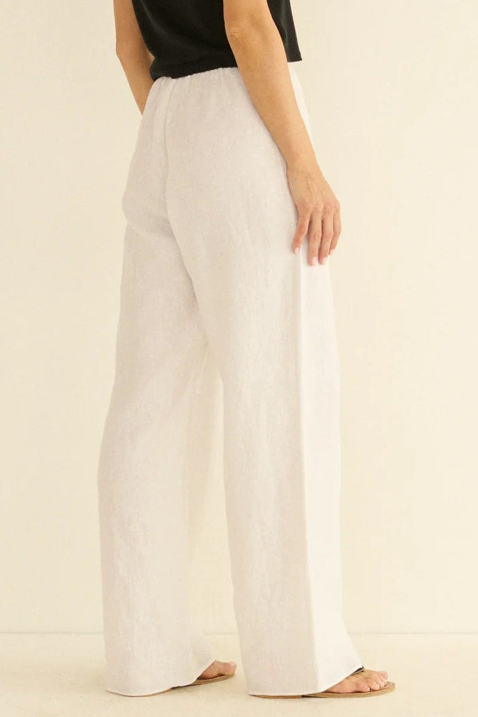 Woman wearing a black top and white pants on a beige background