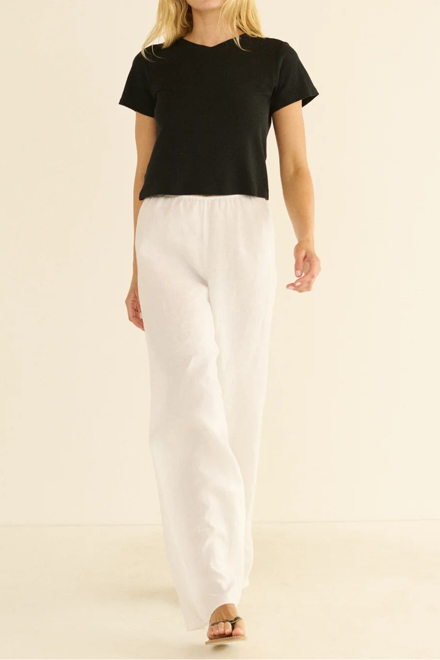 Woman wearing a black t-shirt and white pants on a beige background