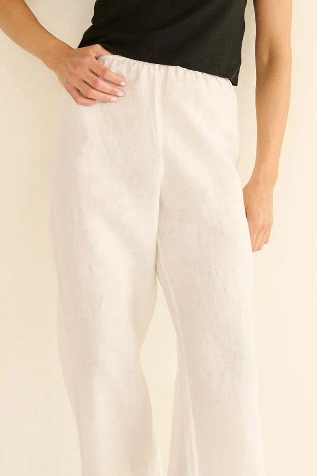 Woman wearing a black t-shirt and white pants against a beige background