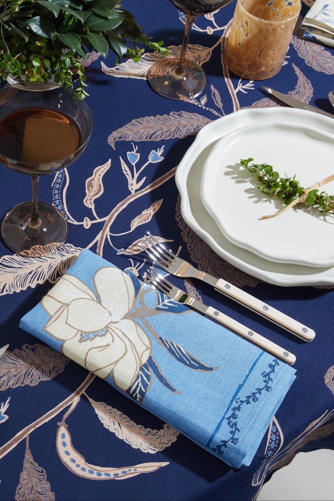 Dining table setting with blue tablecloth, white plates, and silverware.
