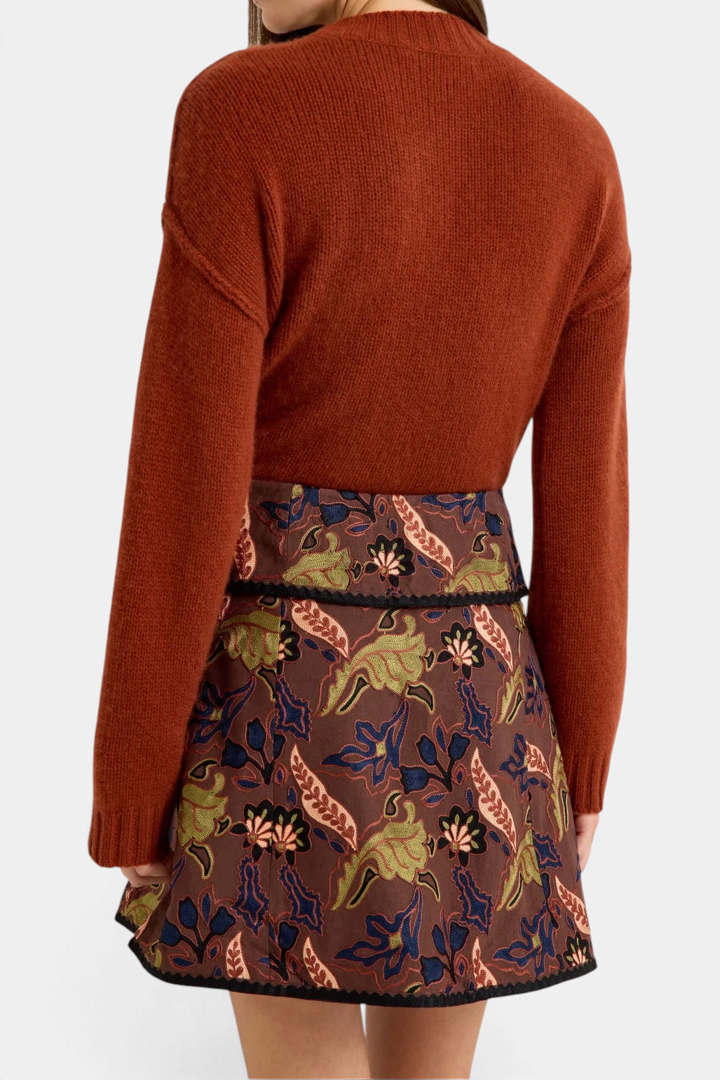Marie Oliver  Ozzie Sweater in rust cashmere worn with a floral patterned skirt, back view.