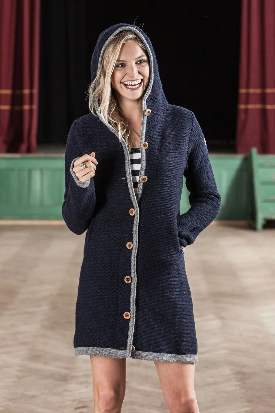 Woman in a navy blue coat standing in an auditorium with red curtains and a chandelier.