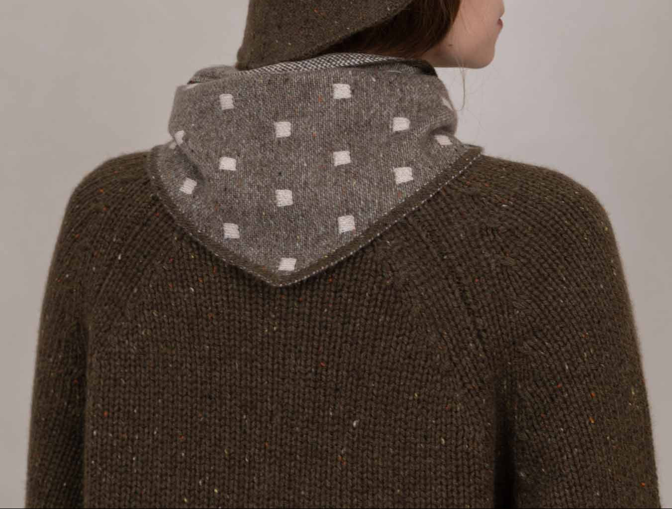 A person shown from the back wearing a brown textured knit hooded sweater with a gray patterned inner hood lining, against a plain light gray background.
