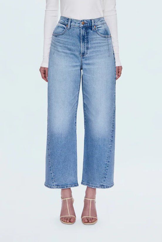 Woman wearing a white long-sleeve top and light blue jeans on a white background