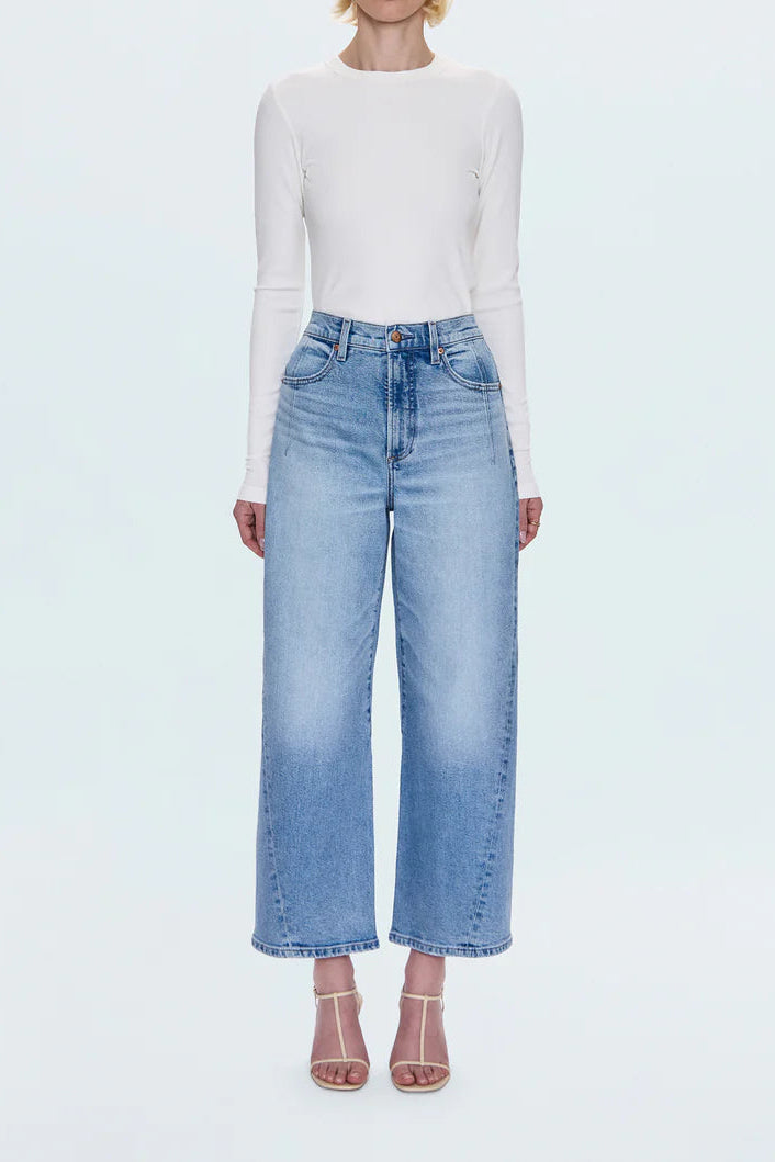 Woman wearing a white long-sleeve top and light blue jeans on a white background