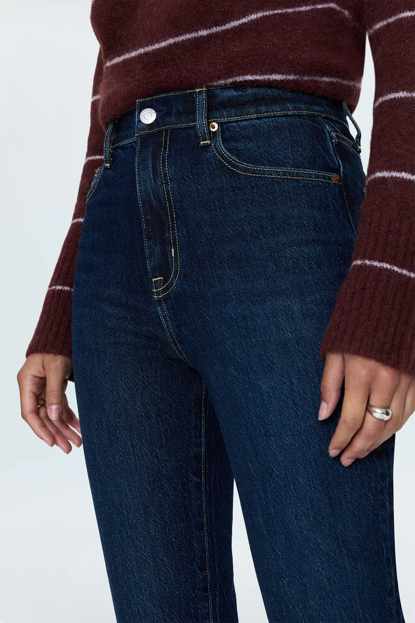 Close-up of a person wearing dark blue high-rise jeans and a burgundy sweater with thin white horizontal stripes, cropped from the chest down against a light gray studio background.